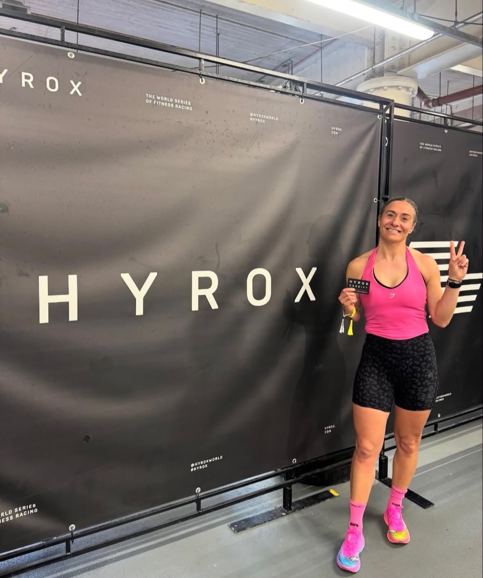 Tash Thornton smiling at a HYROX event in a pink top, holding her race badge